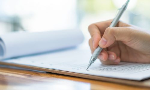 Hand with pen over application form . Hand with pen over application form